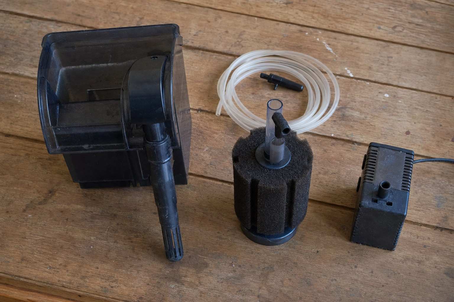 Different aquarium filter types laid out on a wooden table: a hang-on-back filter, a sponge filter, an internal filter